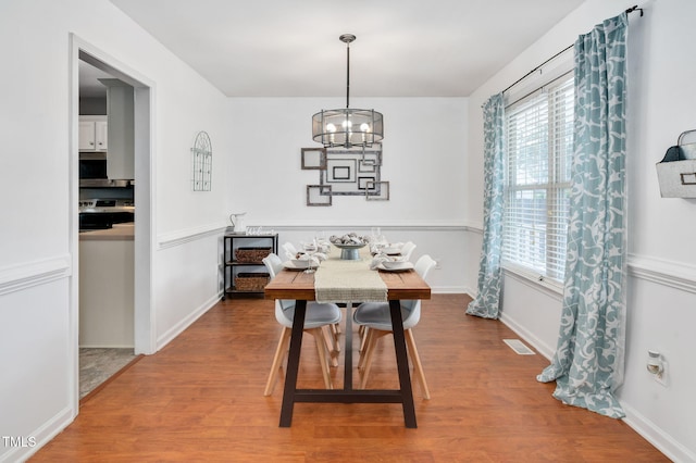 dining area with wood finished floors, a chandelier, healthy amount of natural light, and baseboards