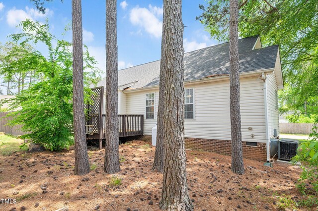 view of side of home with a wooden deck, crawl space, central AC, fence, and roof with shingles