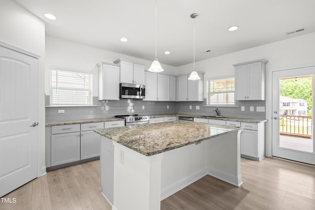 kitchen featuring stainless steel appliances, light wood-type flooring, a sink, a center island, and decorative backsplash