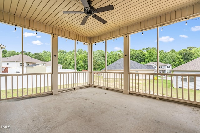 unfurnished sunroom with ceiling fan, a residential view, and view of scattered trees