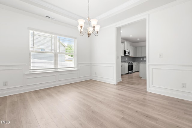 empty room with a chandelier, light wood-style flooring, a wainscoted wall, a decorative wall, and crown molding