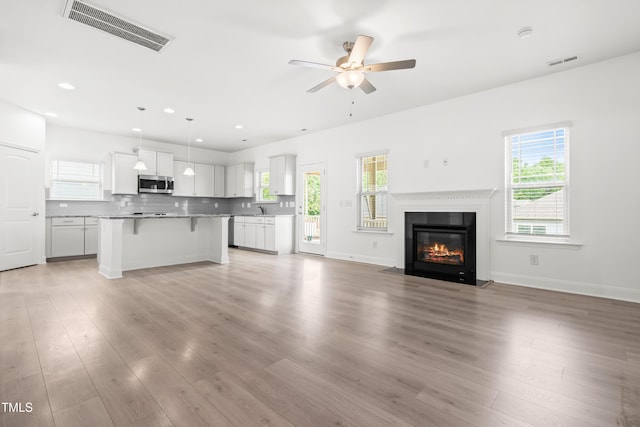 unfurnished living room with ceiling fan, a sink, light wood finished floors, a fireplace with flush hearth, and recessed lighting