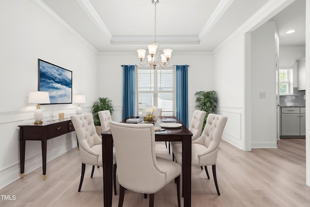 dining area featuring a chandelier, light wood-style floors, a raised ceiling, and crown molding
