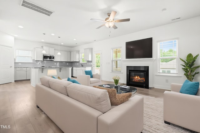 living room with a ceiling fan, a glass covered fireplace, light wood finished floors, recessed lighting, and baseboards