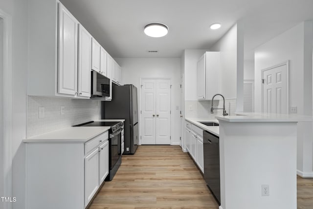 kitchen featuring appliances with stainless steel finishes, light wood finished floors, a peninsula, and white cabinets