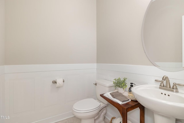 bathroom with toilet, tile patterned flooring, wainscoting, and a sink