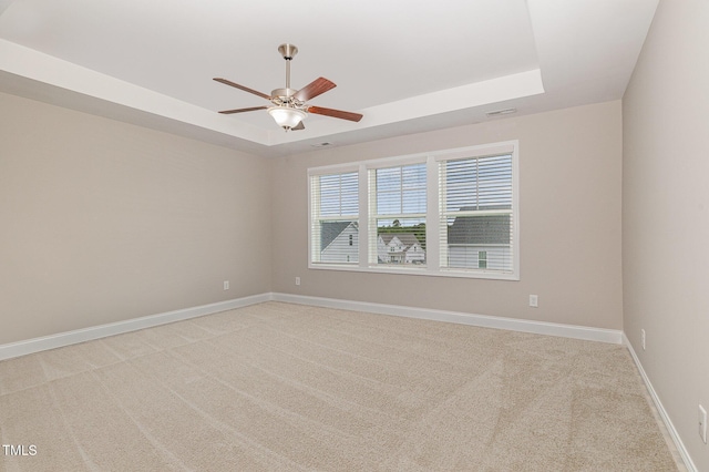 unfurnished room with a tray ceiling, ceiling fan, light carpet, and baseboards