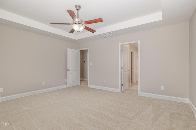 unfurnished bedroom featuring a tray ceiling, light colored carpet, baseboards, and visible vents