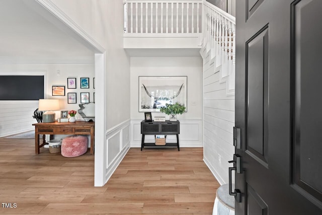 foyer entrance with light wood-style flooring, a high ceiling, and wainscoting