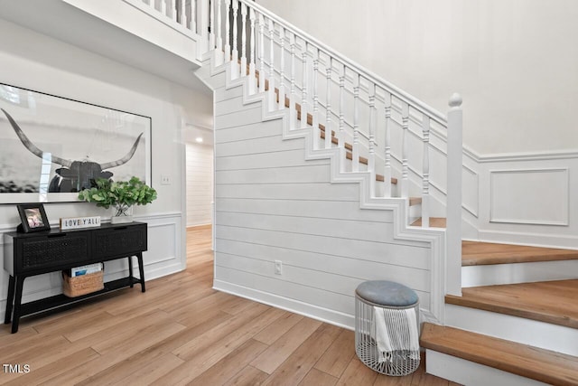 staircase with wood finished floors, a wainscoted wall, and a decorative wall