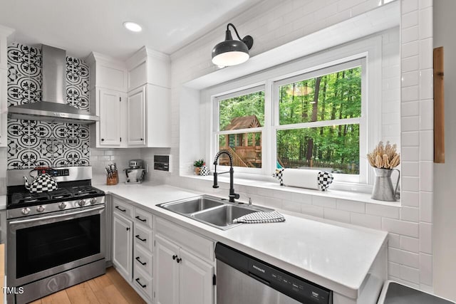 kitchen featuring stainless steel appliances, wall chimney range hood, a sink, light countertops, and tasteful backsplash
