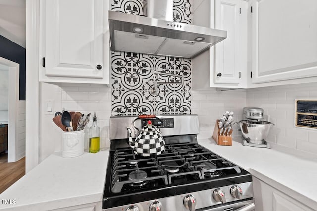 kitchen with stainless steel gas range, ventilation hood, white cabinets, light countertops, and backsplash