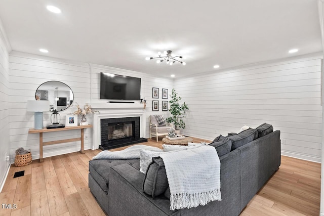 living room with wooden walls, recessed lighting, light wood-type flooring, a fireplace, and crown molding