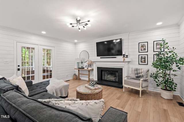 living room with light wood-style flooring, french doors, a glass covered fireplace, wooden walls, and ornamental molding