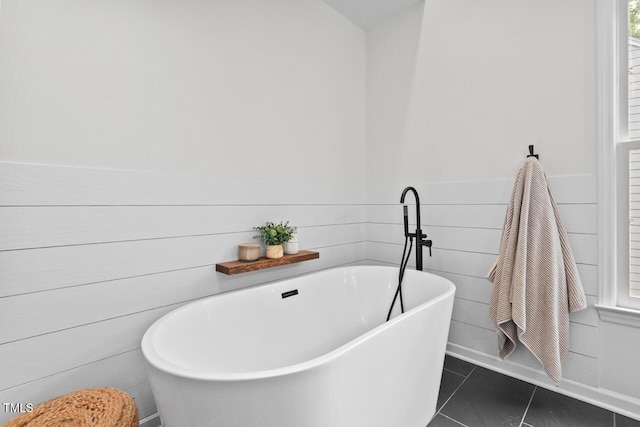 full bathroom featuring a soaking tub, a wainscoted wall, and tile patterned floors