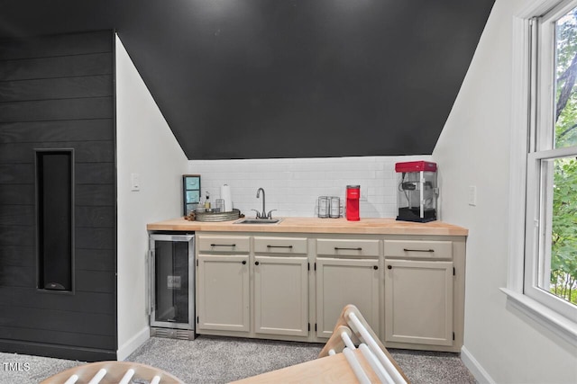 indoor wet bar with beverage cooler, baseboards, tasteful backsplash, lofted ceiling, and light colored carpet