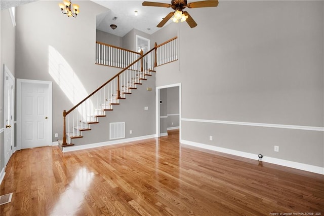 unfurnished living room with visible vents, ceiling fan with notable chandelier, wood finished floors, stairway, and a high ceiling