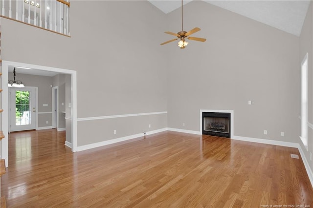 unfurnished living room with light wood-style flooring, ceiling fan with notable chandelier, a fireplace, and high vaulted ceiling