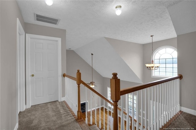 corridor with an upstairs landing, an inviting chandelier, visible vents, and a textured ceiling