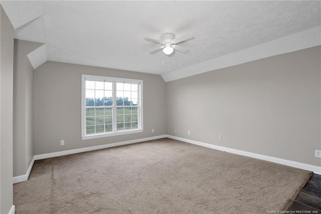 carpeted empty room featuring vaulted ceiling, a textured ceiling, baseboards, and a ceiling fan