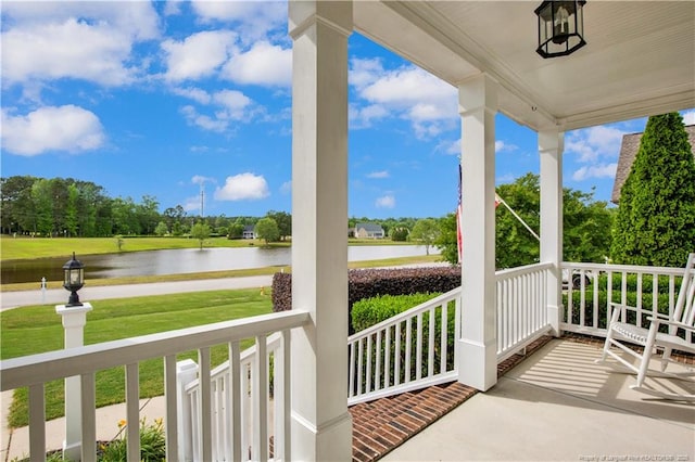 balcony featuring a porch, a water view, and view of wooded area