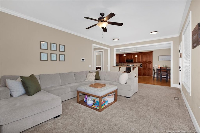 living room with a ceiling fan, ornamental molding, carpet flooring, and baseboards