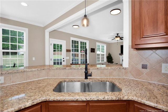 kitchen with a sink, decorative backsplash, healthy amount of natural light, brown cabinetry, and ornamental molding