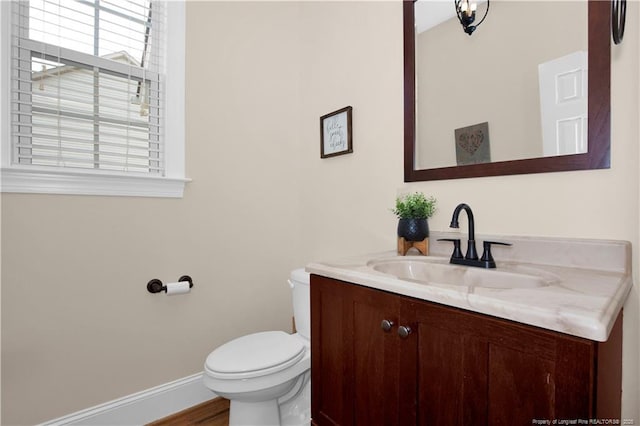 half bath with toilet, vanity, baseboards, and wood finished floors