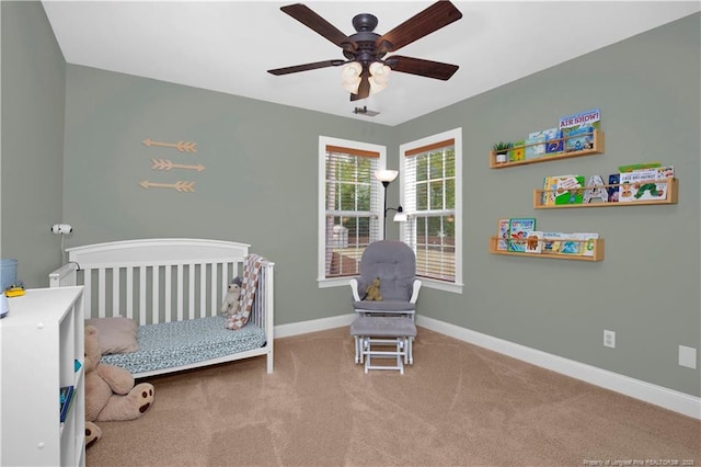 bedroom with a crib, carpet, baseboards, and ceiling fan