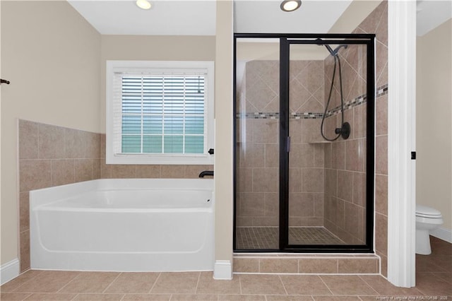 bathroom with a stall shower, a bath, toilet, baseboards, and tile patterned floors