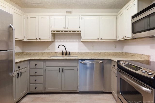 kitchen with a sink, stainless steel appliances, light stone counters, backsplash, and gray cabinetry