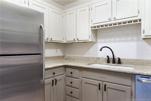 kitchen featuring a sink, stainless steel appliances, white cabinets, light stone countertops, and tasteful backsplash