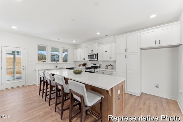 kitchen featuring stainless steel appliances, a breakfast bar area, white cabinetry, a kitchen island, and light wood-style floors