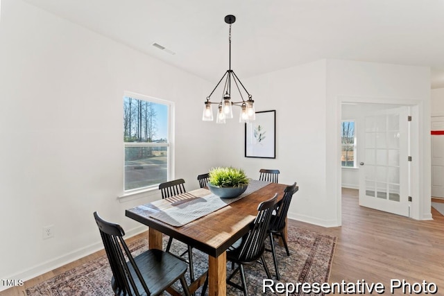 dining space featuring baseboards, a notable chandelier, visible vents, and light wood-style floors