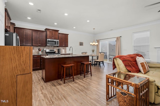 kitchen with stainless steel appliances, a sink, a kitchen bar, open floor plan, and light wood-style flooring