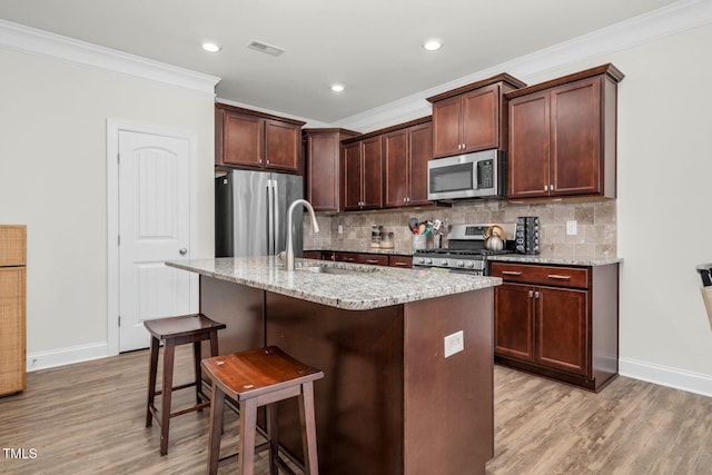 kitchen with appliances with stainless steel finishes, a sink, baseboards, ornamental molding, and light wood-style floors