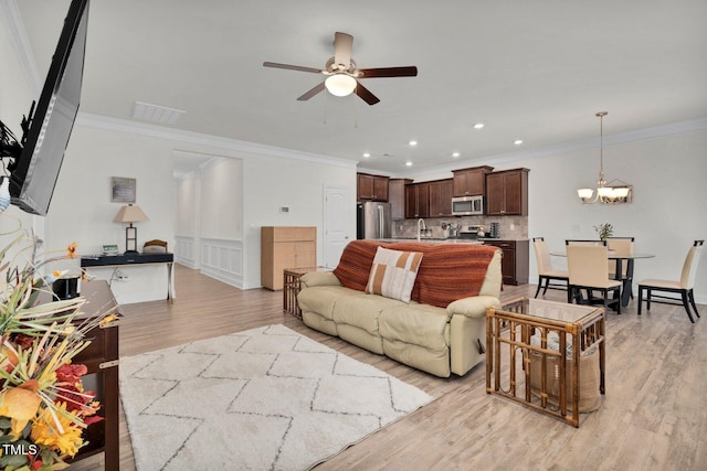 living room with light wood-type flooring, ceiling fan, crown molding, a chandelier, and recessed lighting