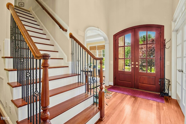 foyer with light wood-style floors, stairway, french doors, and a towering ceiling
