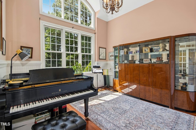 living area featuring a high ceiling, a chandelier, a wainscoted wall, and wood finished floors
