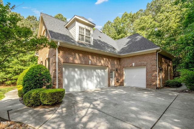 view of property exterior featuring roof with shingles, a garage, brick siding, and driveway