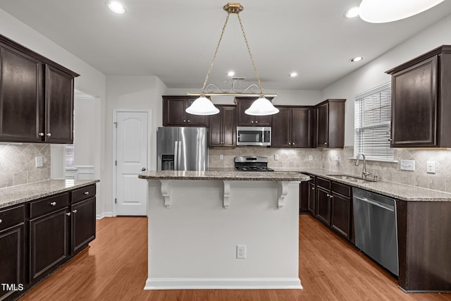 kitchen with stainless steel appliances, a sink, a kitchen breakfast bar, light wood-style floors, and light stone countertops