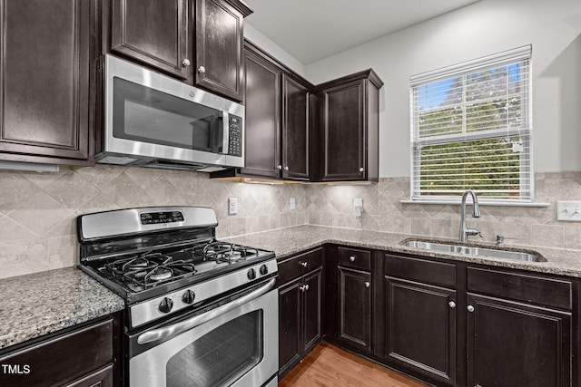 kitchen with stainless steel appliances, a sink, light stone counters, dark brown cabinetry, and light wood-type flooring