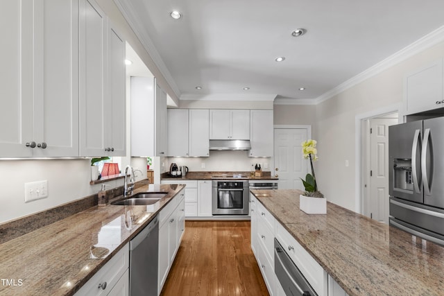 kitchen featuring appliances with stainless steel finishes, a sink, under cabinet range hood, ornamental molding, and white cabinetry