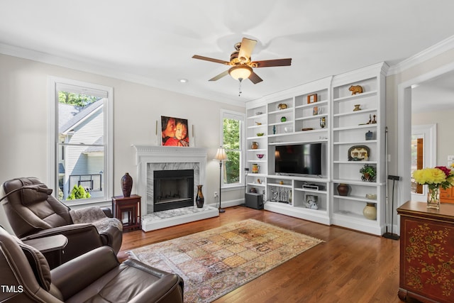living room with plenty of natural light, ceiling fan, crown molding, a high end fireplace, and wood finished floors