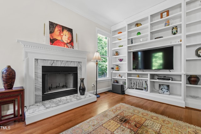 living room with wood finished floors, a high end fireplace, ornamental molding, built in features, and baseboards