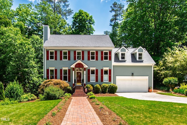colonial house featuring driveway, a chimney, a front lawn, and an attached garage