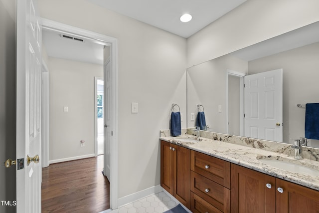 full bath featuring baseboards, double vanity, and wood finished floors