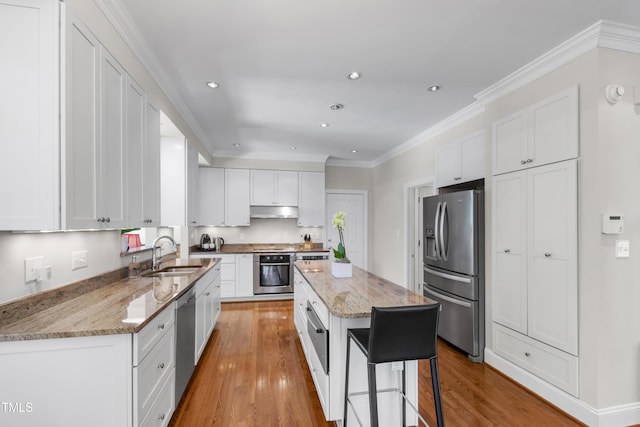 kitchen featuring appliances with stainless steel finishes, a sink, under cabinet range hood, light wood-type flooring, and recessed lighting