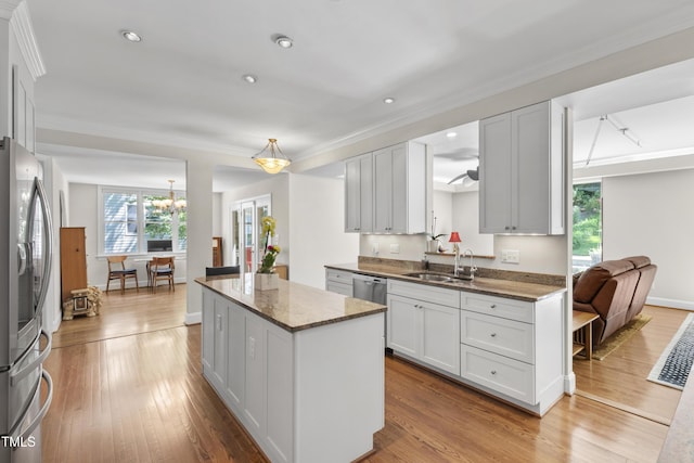 kitchen with stainless steel appliances, a sink, a kitchen island, wood finished floors, and dark stone counters