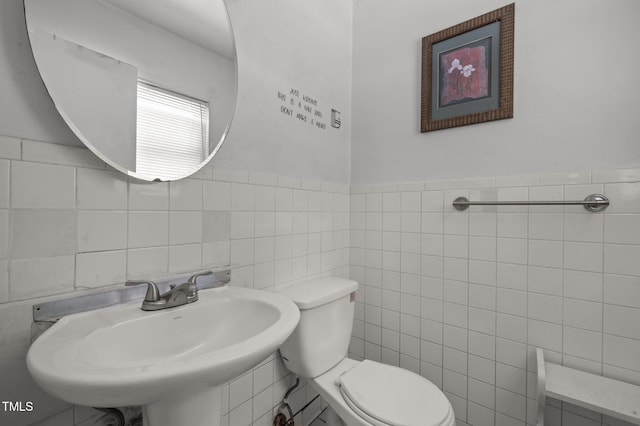 bathroom featuring tile walls, toilet, and a sink